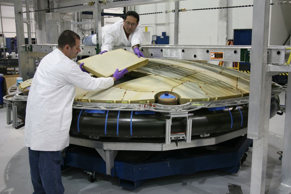 Two technicians in white lab coats assembling a large circular industrial equipment component inside a manufacturing facility.